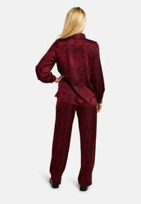 Burgundský saténový dvojdielny set pozostávajúci z blúzky s golierom a dlhými rukávmi s potlačou, doplnený voľnými nohavicami rovnakej farby.