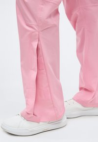 Ροζ παντελόνι με ρυθμιζόμενα πλαϊνά ανοίγματα με βέλκρο, φορεμένο με λευκά αθλητικά παπούτσια σε ανοιχτό φόντο.