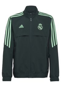 Chaqueta verde oscura con acentos en verde claro y tres franjas en cada manga. Cuenta con un cuello alto y el logo del Real Madrid en el pecho.