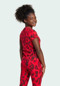 Camiseta de estampado animal rojo con mangas cortas y leggings a juego. Tela elástica con una textura suave y manchas negras en contraste.