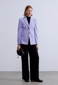 Λιλά σακάκι με γιακάδες με εγκοπές, εσωτερικό κούμπωμα με ένα κουμπί και δύο τσέπες, συνδυασμένο με μαύρο παντελόνι φαρδύ και μαύρη τσάντα. Λείο ύφασμα.