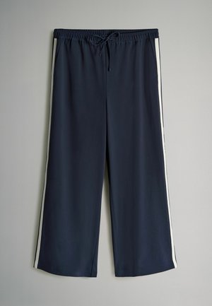 Marinede blå sportsbukser med hvide sidestropper, elastisk talje og snøre. Løs pasform og letvægtigt stof for komfort.