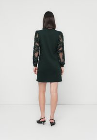 Dark green dress with sheer sleeves featuring textured floral accents, knee-length, simple round neckline, and relaxed fit.