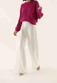 Fuksjowy sweter z dzianiny o szerokich rękawach, zestawiony z białymi spodniami o szerokich nogawkach oraz przezroczystymi szpilkami. Gładka faktura, luźny krój.