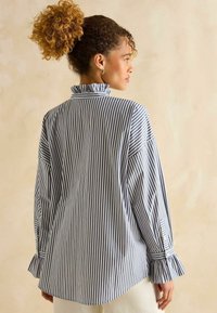 Tumedate ja valged triibuline pikade varrukatega särk, millel on volangkrae ja randmed, lõdva lõike ning pehme kangatekstuuriga.