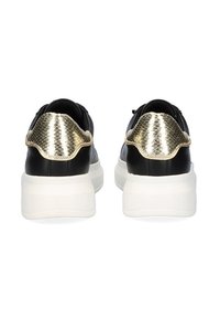 Deportivas negras con una suela blanca, que presentan un acento en el talón de metal dorado texturizado y un material de cuero suave.