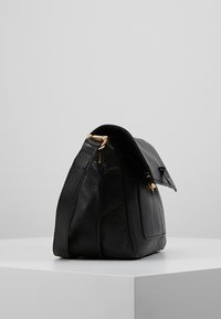 Schwarze Lederhandtasche mit strukturiertem Finish, einer klaren Form und goldenen Hardware-Details. Verfügt über eine umklappbare Klappe und einen Reißverschluss.