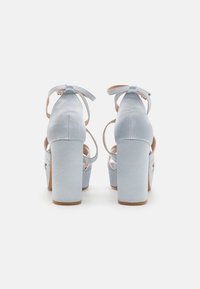 Sandales à talons hauts bleu clair avec une texture lisse, dos ouvert, brides autour de la cheville et talons blocs épais. Design élaboré des brides à l'avant.