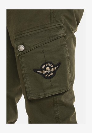 Pantalon cargo vert olive avec une poche à rabat fermée par un bouton en métal et un écusson Von Dutch représentant un crâne avec des ailes.