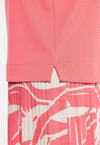 Top rosa lavorato a maglia con un motivo a spina di pesce testurizzato e un piccolo orlo a V, sovrapposto a una gonna a pieghe con un design astratto bianco e rosa.