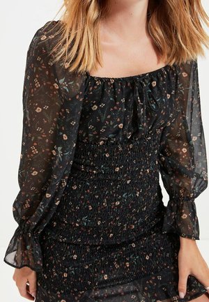 Zwarte chiffon top met bloemenpatroon en lange mouwen, met een ingezamelde, smock taille. De patronen bevatten kleine bloemen en bladeren in gedempte kleuren.