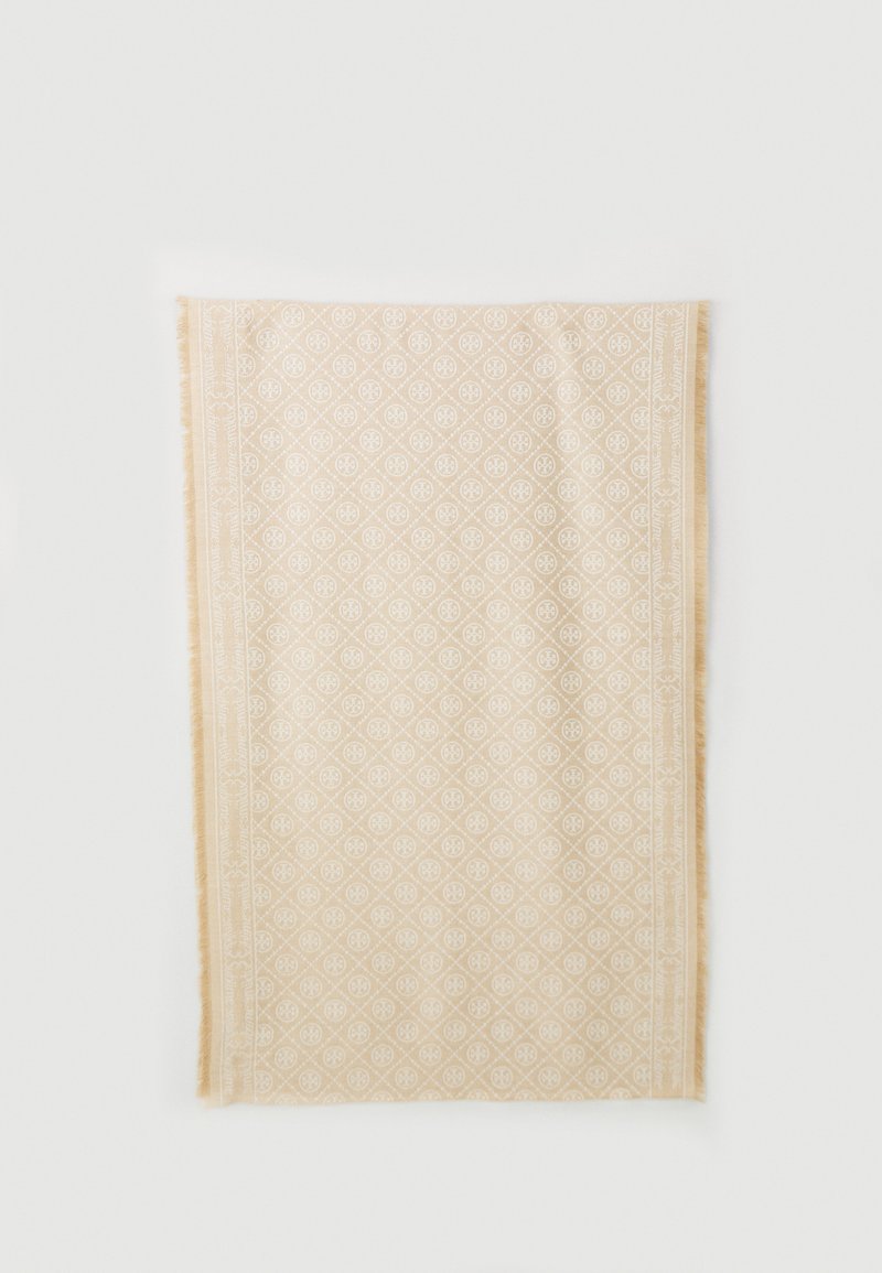 Vaalean beige suorakulmainen tekstiili, jossa on valkoinen geometrinen kuvio ja hapsureunat, asetettuna litteänä valkoiselle pinnalle.