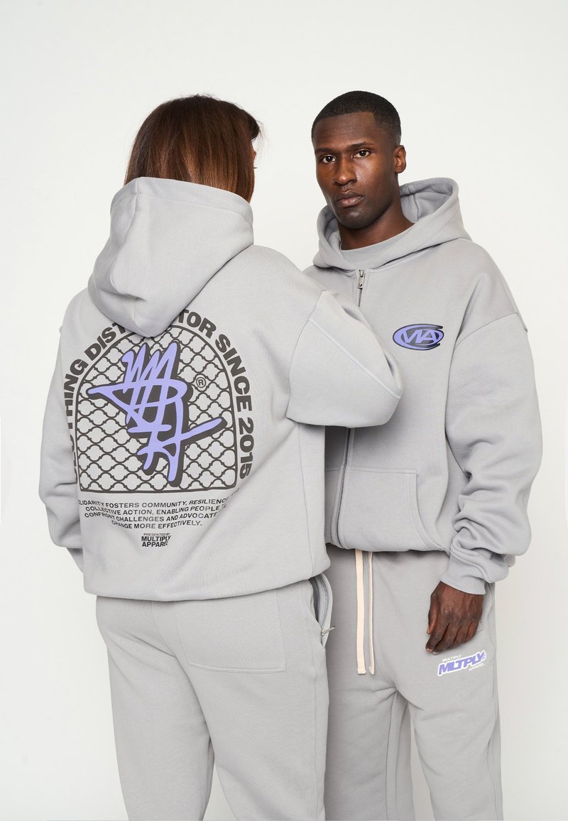 Felpe con cappuccio grigie con zip frontale, caratterizzate da stampe grafiche sulla schiena e sul petto, abbinate a jogger grigi coordinati.