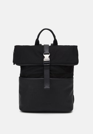Mochila negra con solapa plegable asegurada con correa de cuero y hebilla metálica, con asa superior y sección inferior de cuero liso.