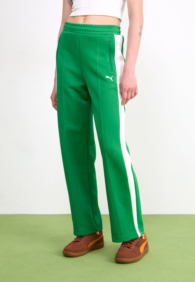 Grønne sweatpants med en hvid stribe ned ad siden, lavet af blødt stof med snoretræk i livet og lynlåslommer. Brune sneakers fuldender looket.