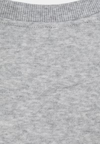 Primer plano de un tejido de punto gris claro con cuello de canalé y costuras visibles en una prenda.