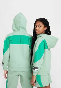 Grön hoodie med kontrasterande teal-accenter och svart "AIR"-text. Tillverkad av mjukt tyg; har en rymlig huva och ribbade ärmslut.