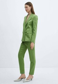 Groene linnen blazer en broek, slim fit, met een enkele knoopsluiting, zijzakken, gecombineerd met lichtgrijze, puntige muiltjes.