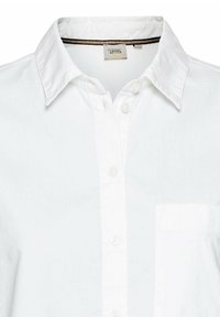 Chemise blanche à boutons en tissu léger, avec un col rabattu, une poche poitrine unique et un détail textural subtil.