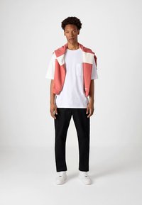 Krótki rękaw biała koszulka z kieszenią, czarne zwężane spodnie oraz różowy sweter narzucony na ramiona, uzupełnione białymi tenisówkami.