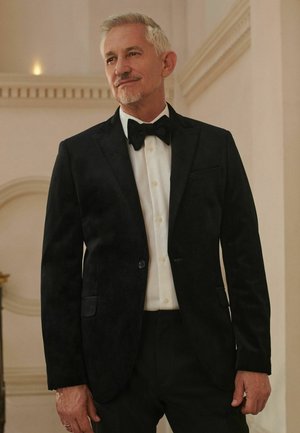 Schwarze Samt-Tuxedojacke mit satinierten Revers, getragen über einem weißen Hemd und einer Fliege. Besitzt einen einzelnen Knopfverschluss und Seitentaschen.