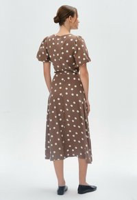 Braunes Kleid mit Polka-Dots, kurzen Puffärmel, tailliertem Schnitt und einem knielangen Rock, kombiniert mit schwarzen Slippern.