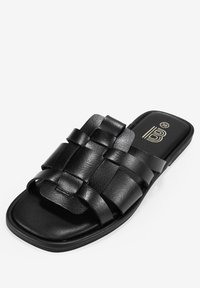 Sandale glissante en cuir noir avec un design de bride tissée, forme de orteil carrée, semelle plate et branding minimal sur la semelle intérieure. Taille 36.