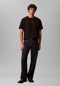 Must valge logoga T-särk, tumedate siniste sirge säärega teksadega. Komplekti lõpetavad musta nahast kingad.