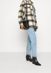 Persona che indossa una giacca a quadri beige e nera, jeans azzurri chiari, stivaletti neri con tacco e porta una borsa a tracolla in pelle nera.