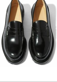 Crne kožne loferice s sjajnim finišom, sa detaljnim šavovima, okruglim vrhom i debelim đonom. Akcentni pojas preko vrha s valovitim rubovima.
