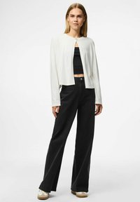 Vit kortärmad cardigan med långa ärmar och rund halsringning, kombinerad med högmidjade svarta vida jeans och ljusa sneakers.