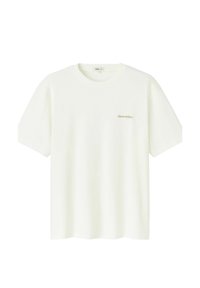 T-shirt en coton beige clair à manches courtes et col rond. Présente une petite inscription dorée "Gros caillou" sur le devant.