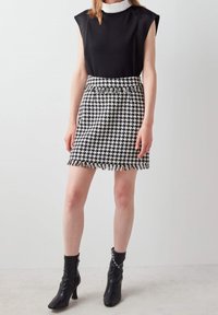Top negro sin mangas con hombreras, combinado con una mini falda de pata de gallo en blanco y negro con dobladillo de flecos y cinturilla elástica. Botines negros.