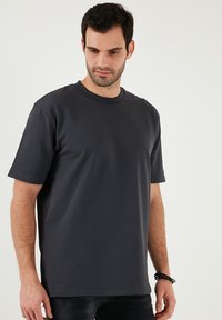 Tmavě šedé tričko s kulatým výstřihem, vyrobené z hladké bavlněné tkaniny, s krátkými rukávy a volným střihem. Minimalistický design bez vzorů.