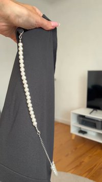 Vêtement noir maintenu par une chaîne reliée à des perles en verre. Les détails notables comprennent une texture lisse et un fermoir métallique sur la chaîne.