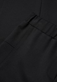 Zwarte stof met een gladde textuur, voorzien van een elastische tailleband en zijzakdetail, ontworpen in een aansluitende stijl.