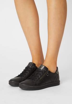 Des baskets en cuir noir avec un design à lacets, des accents métalliques, un détail de fermeture éclair sur le côté et une semelle en caoutchouc texturée.