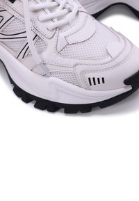 Sneaker atletico bianco con upper in rete, accenti neri, suola testurizzata e zone rinforzate. Presenta un sistema di lacci e un colletto imbottito.