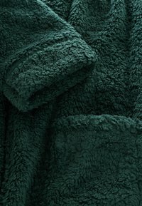 Nahaufnahme eines dunkelgrünen, strukturierten Fleece-Stoffs mit einer weichen, flauschigen Oberfläche und gefalteten Lagen.