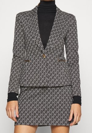 Donna che indossa una giacca con motivo geometrico bianco e nero e gonna coordinata sopra una maglia dolcevita nera.