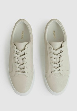 Kerged beige nahkist tenniset tekstuuriga viimistlusega, millel on kuus aukku, siledad paelad ja valge kummist tald. Siseosa kuldsete brändingutega.