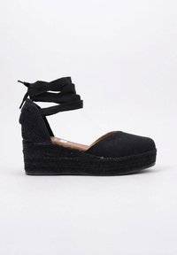 Zapato de cuña de espadrille negro con parte superior de tela texturizada, mediados de yute trenzado y lazos en el tobillo. Diseño de punta redonda y suela de goma plana.