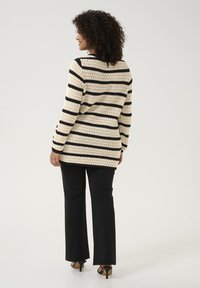 Cream and black striped knit sweater, long sleeves, loose fit, with intricate textured pattern; paired with black, slim straight pants and heels.