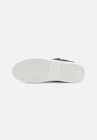 Tengerészeti stílusú sneaker texturált vászon felsőrésszel, fehér gumitalppal és rugalmas futómintázattal. Feliratozás a lapon.