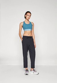 Sportbeha in teal met grijze band; lichtgewicht zwarte joggers met verstelbare trekkoord; witte en zwarte sportschoenen.