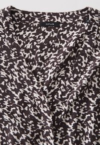 Blusa a righe in bianco e nero con scollatura a V, realizzata in un tessuto leggero e strutturato. Etichetta del marchio visibile sul colletto.