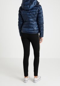 Laivastonsininen toppatakki hupulla, jossa on vaakasuunnassa tikattu kuvio ja kiiltävä pinta. Yhdistetty mustiin legginsseihin ja valkoisiin lenkkareihin.