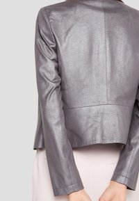 Veste courte gris métallique à manches longues, texture lisse et coutures minimales. Présente une coupe propre et moderne à la taille.