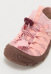 Różowe siatkowe sneakersy z brązową gumową podeszwą. Posiadają elastyczne sznurówki, zapięcie do regulacji oraz przeszywane detale w górnej części.