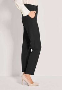 Schwarze maßgeschneiderte Hosen mit einem glatten Finish, ausgestattet mit Seitentaschen und einem geraden Bein. Ergänzt durch beige High Heels.